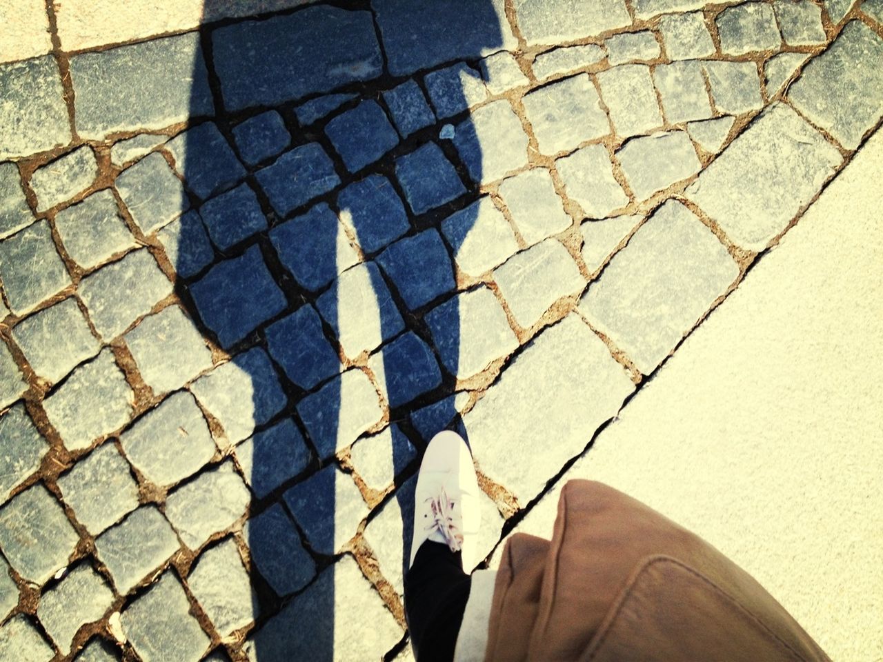 high angle view, street, cobblestone, paving stone, low section, sidewalk, standing, shadow, lifestyles, road marking, pattern, footpath, day, outdoors, person, sunlight, men, unrecognizable person