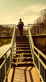 Man standing on footbridge against sky