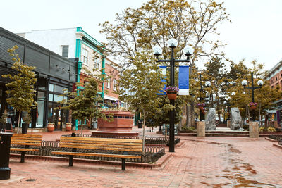 Empty bench by street in city against clear sky