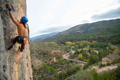 Shirtless man rock climbing against sky