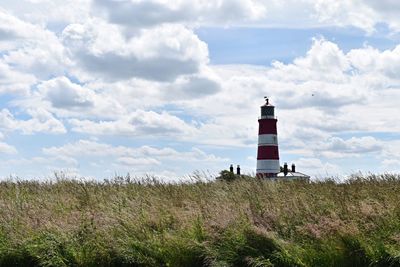 Lighthouse on field against cloudy sky