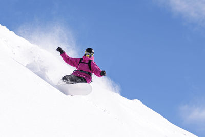 Man with arms outstretched snowboarding on snowy mountains under blue sky