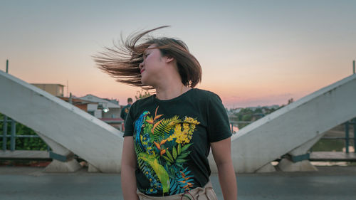 Woman tossing hair against sky during sunset