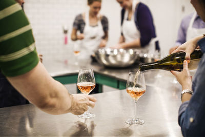 Cropped image of woman pouring wine while standing by coworkers at commercial kitchen