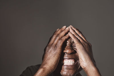 Smiling elderly man covering face over white background