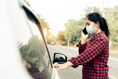 Young woman holding camera while standing in car