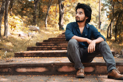 Young man looking away while sitting on tree