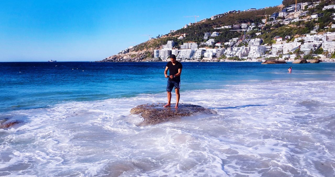 water, sea, full length, lifestyles, leisure activity, blue, rear view, vacations, beach, clear sky, standing, person, shore, casual clothing, men, wave, sky, weekend activities