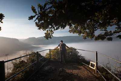 Man standing by railing on mountain against sky