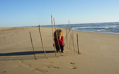 Child playing amidst sticks at beach against clear sky