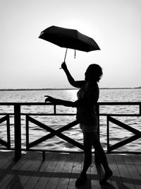 Woman holding umbrella while standing by railing against sea