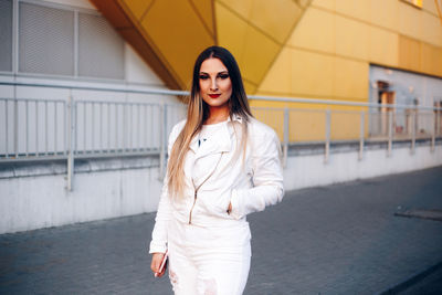 Portrait of beautiful young woman standing against building