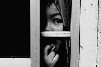 Portrait of boy with finger in mouth looking through window