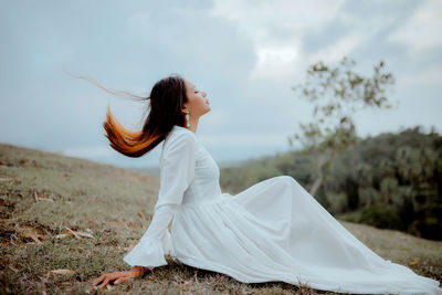 Side view of woman sitting on grass against sky