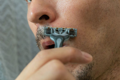 Close-up midsection of man shaving mustache at home