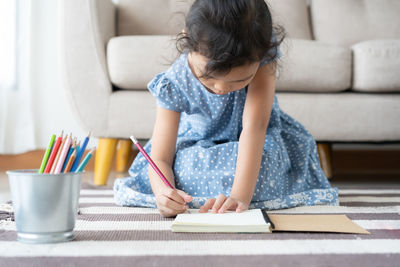 Girl writing in book while sitting on rug at home