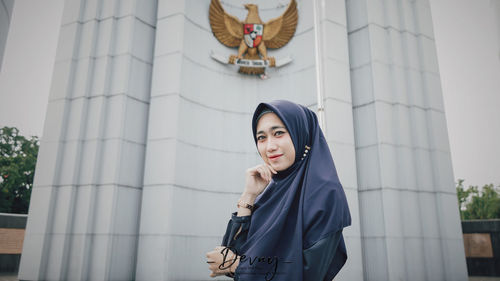 Portrait of woman standing against building in city