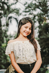 Portrait of smiling young woman standing against trees