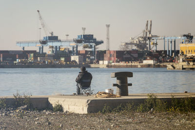 Rear view of man sitting on pier at harbor