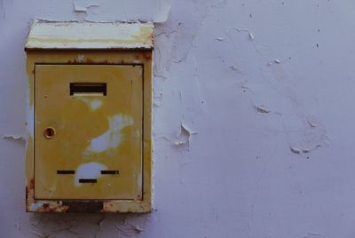 Close-up of yellow mailbox on old wall