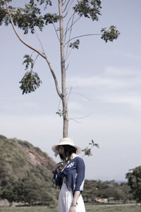 Rear view of woman standing by tree against sky