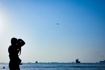 Silhouette man standing at beach against blue sky