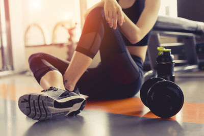 Low section of woman sitting by dumbbells in gym