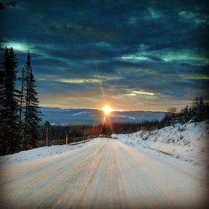 Snow covered road against sky during sunset