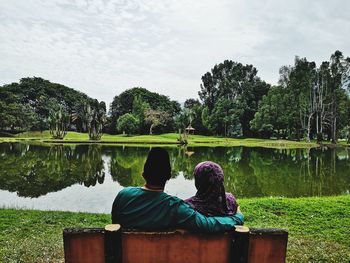 Rear view of couple sitting by lake against sky