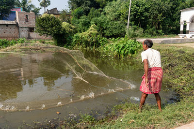 A poor fisherman in a village in west bengal of india is fishing with nets from the pond