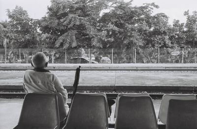 Rear view of senior man sitting at railroad station platform against trees