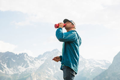 Man drinking water while standing by mountain against clear sky