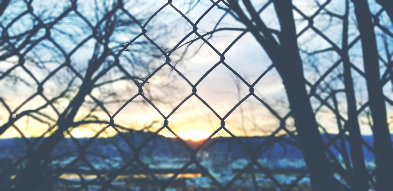 sunlight, sky, reflection, no people, nature, chainlink fence, fence, focus on foreground, sunset, outdoors, cloud, security, tree, day, branch, protection, metal, tranquility, architecture, light, plant, silhouette, beauty in nature, backgrounds, close-up, built structure