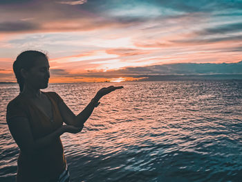 Girl standing by sea against sky during sunset