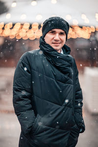 Portrait of man wearing winter coat standing in snow at city street