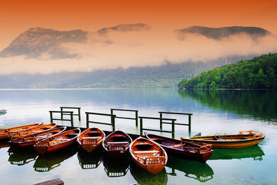 Boats moored in lake against sky during sunset