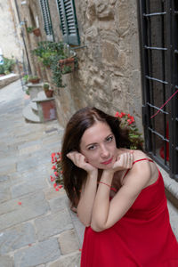 High angle portrait of woman wearing red dress while sitting against building in city