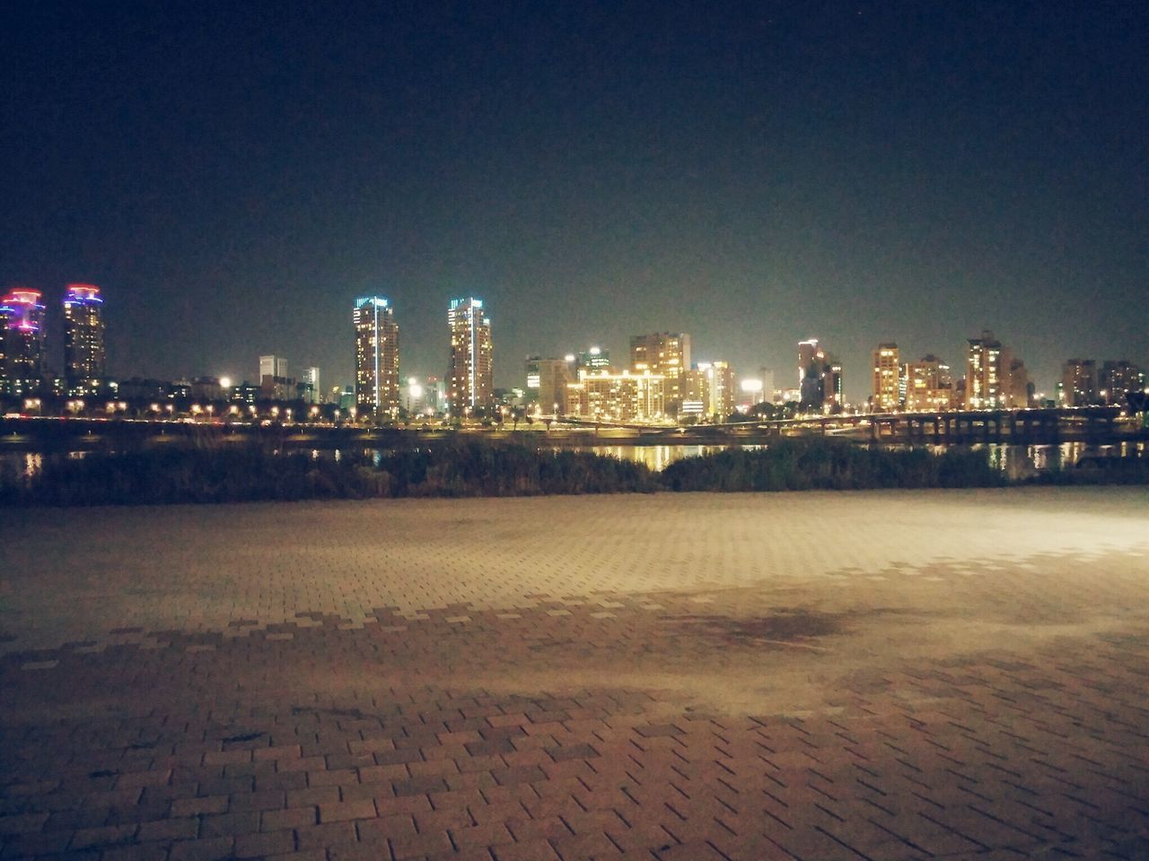 illuminated, night, building exterior, architecture, city, built structure, clear sky, cityscape, copy space, water, skyscraper, river, urban skyline, tall - high, modern, waterfront, sky, sea, tower, reflection