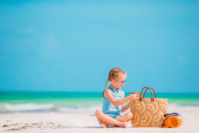 Full length of girl sitting at beach against sky