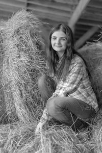 Black and white portrait of young woman sitting on hay bale