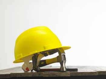 Close-up of hardhat with hammer on table against white background