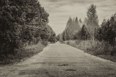 Dirt road amidst trees against sky