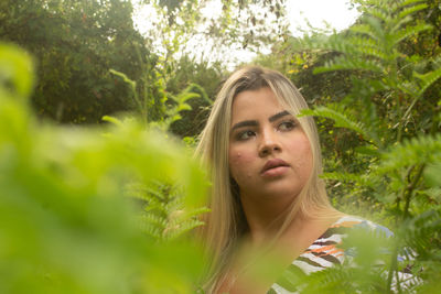 Portrait of young woman looking away against trees