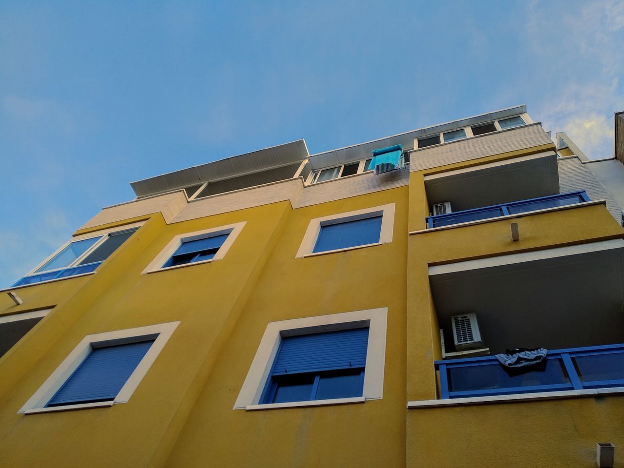 built structure, building exterior, window, architecture, low angle view, sky, building, residential district, yellow, no people, nature, day, city, blue, outdoors, clear sky, in a row, sunlight, apartment, glass - material