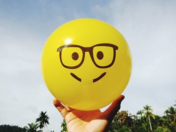 Close-up of hand holding yellow balloons against sky