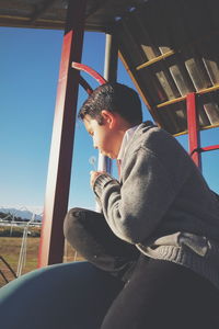 Boy blowing dandelion while siting in playground