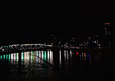 Illuminated buildings by river against sky at night