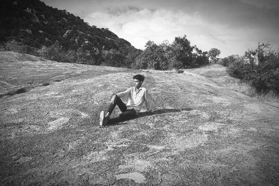 Man sitting on field against sky