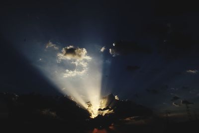 Low angle view of sunlight streaming through clouds