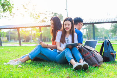 Friends studying while sitting on grassy field at park